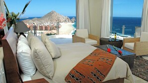 Een hotelkamer met een groot bed, twee fauteuils, een tafeltje en uitzicht op de oceaan en een berg.
