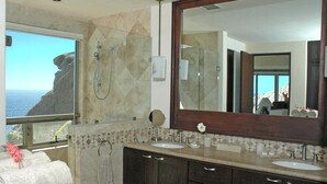 Een badkamer met een grote spiegel, twee wasbakken, een douche en uitzicht op de oceaan.