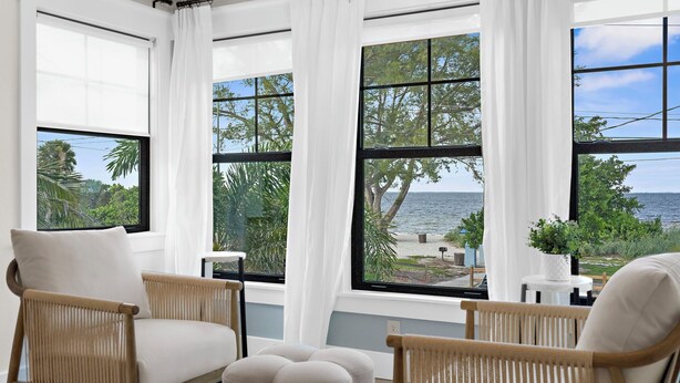 A room with large windows, wicker furniture, and a view of the sea and greenery. - ⚓Bay Dreamin! Walk to the Beach, Pier, & Pine Ave! Heated Pool!⚓⛳🏖🌅 (Anna Maria)
