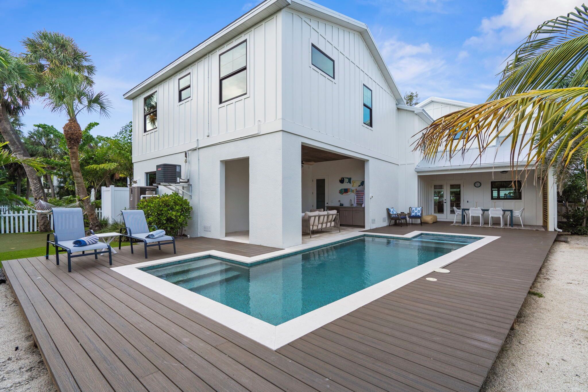 A white two-story house with a wooden deck and a swimming pool.