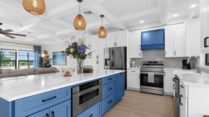 A modern kitchen with white and blue cabinetry, stainless steel appliances, and a large island with a built-in oven. - ⚓Bay Dreamin! Walk to the Beach, Pier, & Pine Ave! Heated Pool!⚓⛳🏖🌅 (Anna Maria)