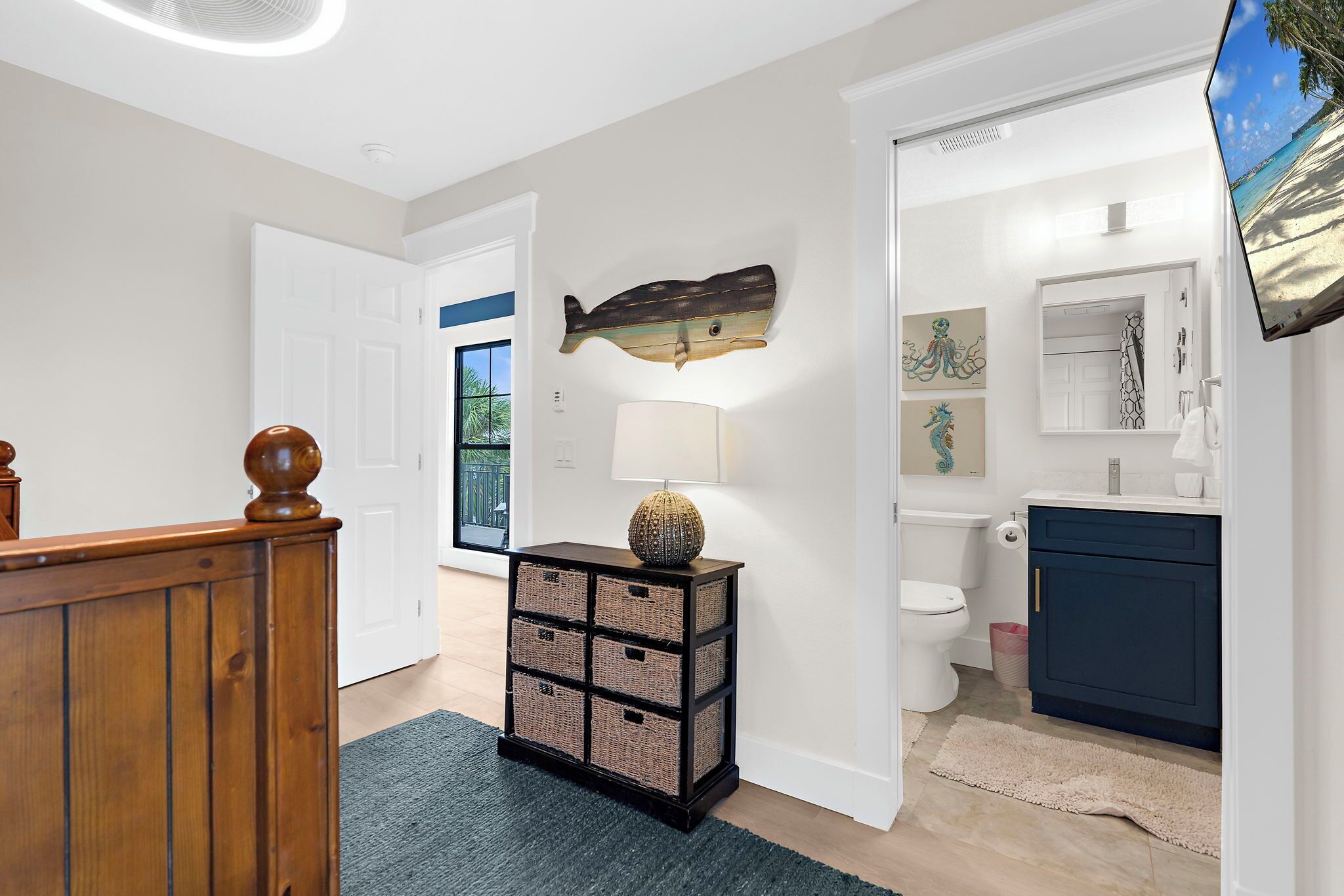 A hallway with a wooden railing, a wall-mounted fish sculpture, a lamp, and a view of a bathroom with a sink and toilet.