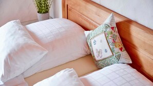 A neatly made bed with white linens and a single decorative pillow with a floral pattern.