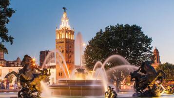 Una fuente con chorros de agua, rodeada de estatuas de caballos y jinetes, con un edificio alto al fondo.