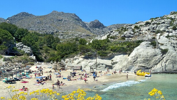 A beach with clear waters, rocky cliffs, and a variety of beach umbrellas and sun loungers. - VILLA TARONGERS - STAY FOR COUPLES (Pollensa)