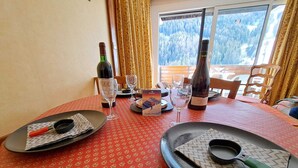 A dining table set with plates, cutlery, wine glasses, and bottles, with a scenic mountain view through a window. - Studio cabin in Pra-Loup with balcony and mountain view (Pra-Loup)