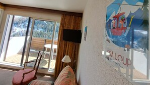 A room with a large window, a television, a chair, and a wall-mounted lamp. - Studio cabin in Pra-Loup with balcony and mountain view (Pra-Loup)