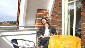 A person sitting on a chair on a balcony with a table covered in a yellow cloth. - Ferienwohnung Sandbank - Haus Ankerplatz am Süderriff in Neuharlingersiel (Neuharlingersiel)