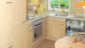 A compact kitchen with wooden cabinets, a built-in oven, and a window with a view of greenery. - Ferienwohnung Sandbank - Haus Ankerplatz am Süderriff in Neuharlingersiel (Neuharlingersiel)