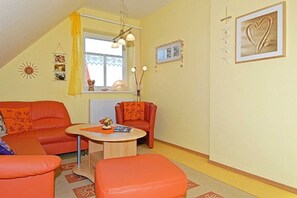 A cozy living room with orange furniture, a small table, and a window with curtains.
