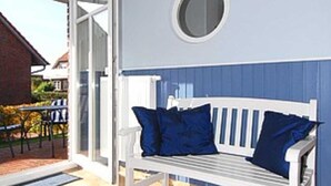 A white bench with blue cushions in a covered outdoor area with a tiled floor and a round window above.