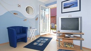 A living room with a blue sofa, a television on a wooden stand, a small table, and a patterned rug.