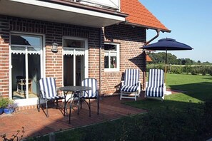 A brick house with a patio area featuring two tables and four striped chairs.