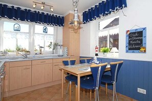 A kitchen with a dining table and chairs, a hanging light fixture, and a window with curtains.