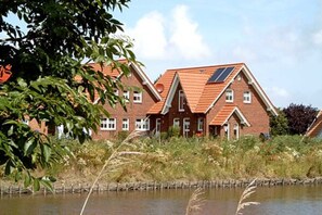 A row of red brick houses with pitched roofs and solar panels, situated by a calm body of water.
