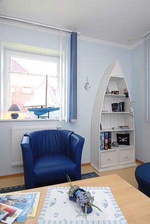 Une pièce avec un fauteuil bleu, une bibliothèque blanche aux lignes courbes et une fenêtre avec des rideaux.