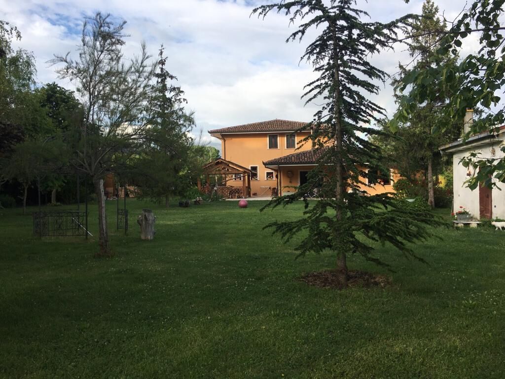 Una casa con un prato curato, un piccolo albero e un gazebo.