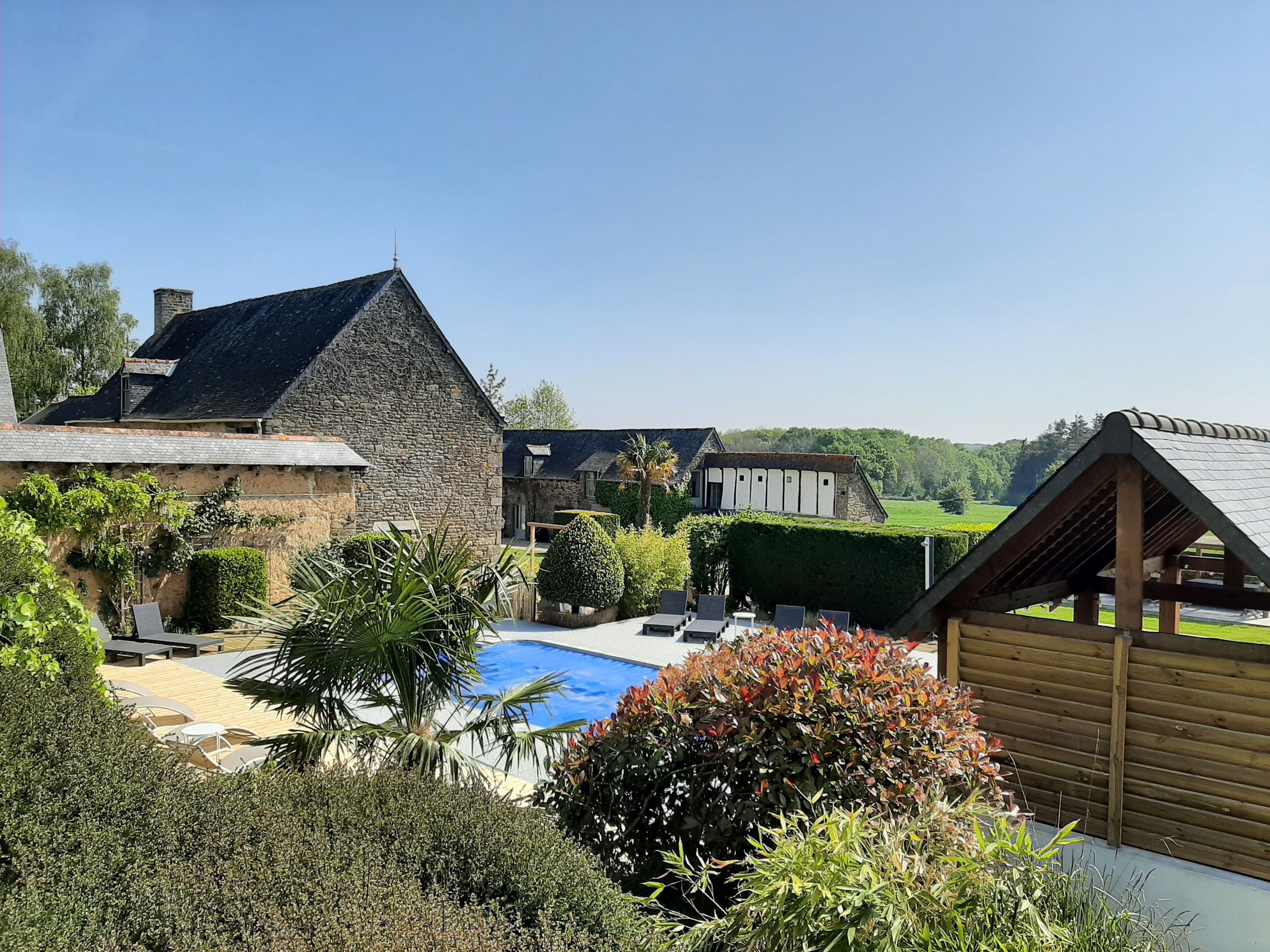 A stone building with a triangular roof, a swimming pool, and a wooden structure.
