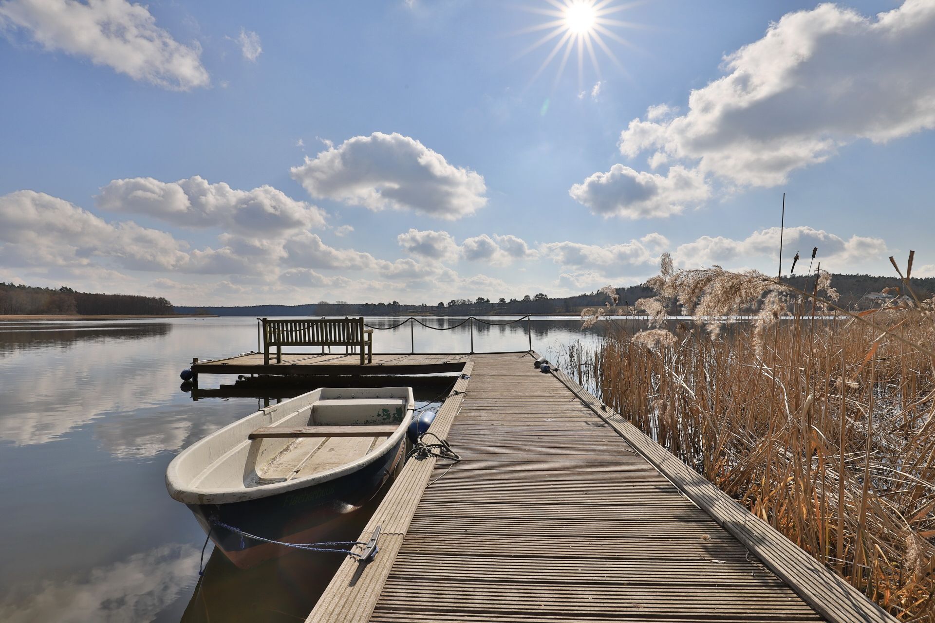 A wooden dock extending into calm water with a bench and a small boat moored at the end.