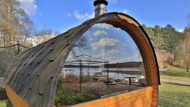 Une structure en bois surmontée d’un dôme de verre, qui reflète la vue sur le lac et où l’on aperçoit un banc et des tables.