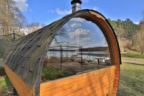 A wooden structure with a glass dome, reflecting a lakeside view with a bench and tables.