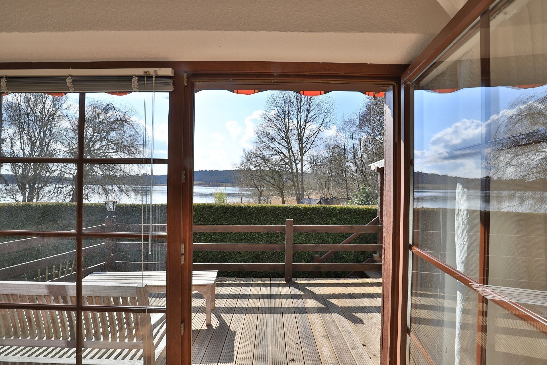 A view from a room with large windows overlooking a wooden deck and a lake.