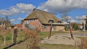 Un bâtiment traditionnel en briques, doté d’un toit de chaume, d’un escalier et d’une balançoire en premier plan.