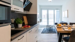 Une cuisine moderne avec des meubles blancs, un plan de travail noir et un coin repas comprenant une table et des chaises en bois.