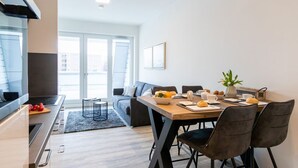Une cuisine moderne avec un coin repas, comprenant une table en bois, des chaises noires et un canapé gris.