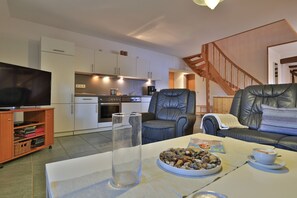 A modern living room with a television, leather armchairs, a coffee table with a bowl of snacks, and a staircase in the background.