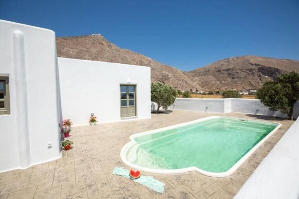 A white building with a swimming pool, a mountain in the background, and a clear sky. - Elixirium Villa with private Swimming pool (Santorini)