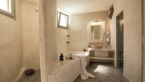 Casa de banho com banheira, lavatório e espelho. É visível uma janela e uma porta.