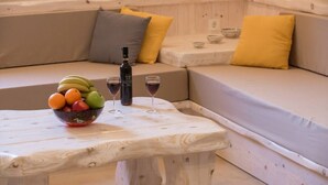 Um espaço de estar acolhedor com uma mesa de madeira, uma cesta de frutas, duas taças de vinho e uma garrafa de vinho.