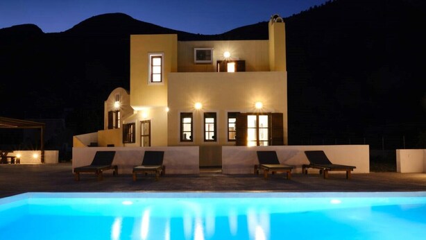 Un bâtiment à deux étages, avec une piscine à l’avant, comprenant des chaises longues et un éclairage extérieur soigné.