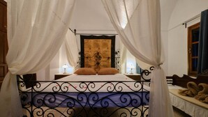 Un lit avec un cadre en métal et des rideaux blancs, une carte accrochée au mur et une table de chevet avec une lampe.