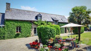 A stone building with ivy-covered walls, a gravel driveway, and outdoor seating with a table and chairs. - In the grounds of a manor house (Saint Hélen)