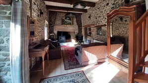 A rustic stone-walled living room with a fireplace, wooden furniture, and a large mirror. - In the grounds of a manor house (Saint Hélen)