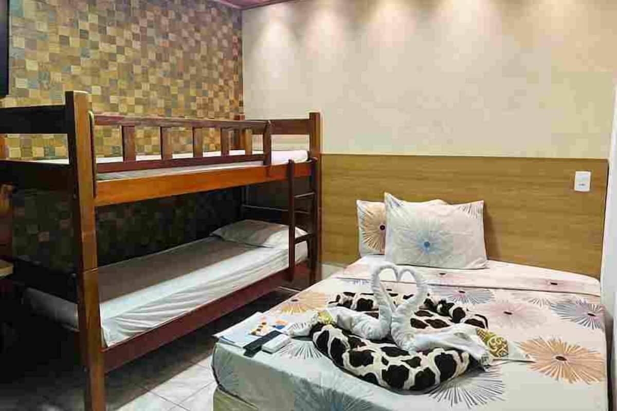 Une chambre avec un lit superposé, une tête de lit en bois, un mur à motifs et un lit recouvert d’une couvre-lit à fleurs et agrémenté d’un coussin en forme de cœur.