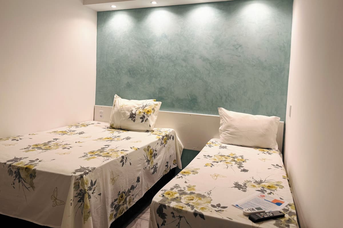 Une chambre d’hôtel avec deux lits, chacun agrémenté de draps à motifs floraux et d’oreillers blancs.