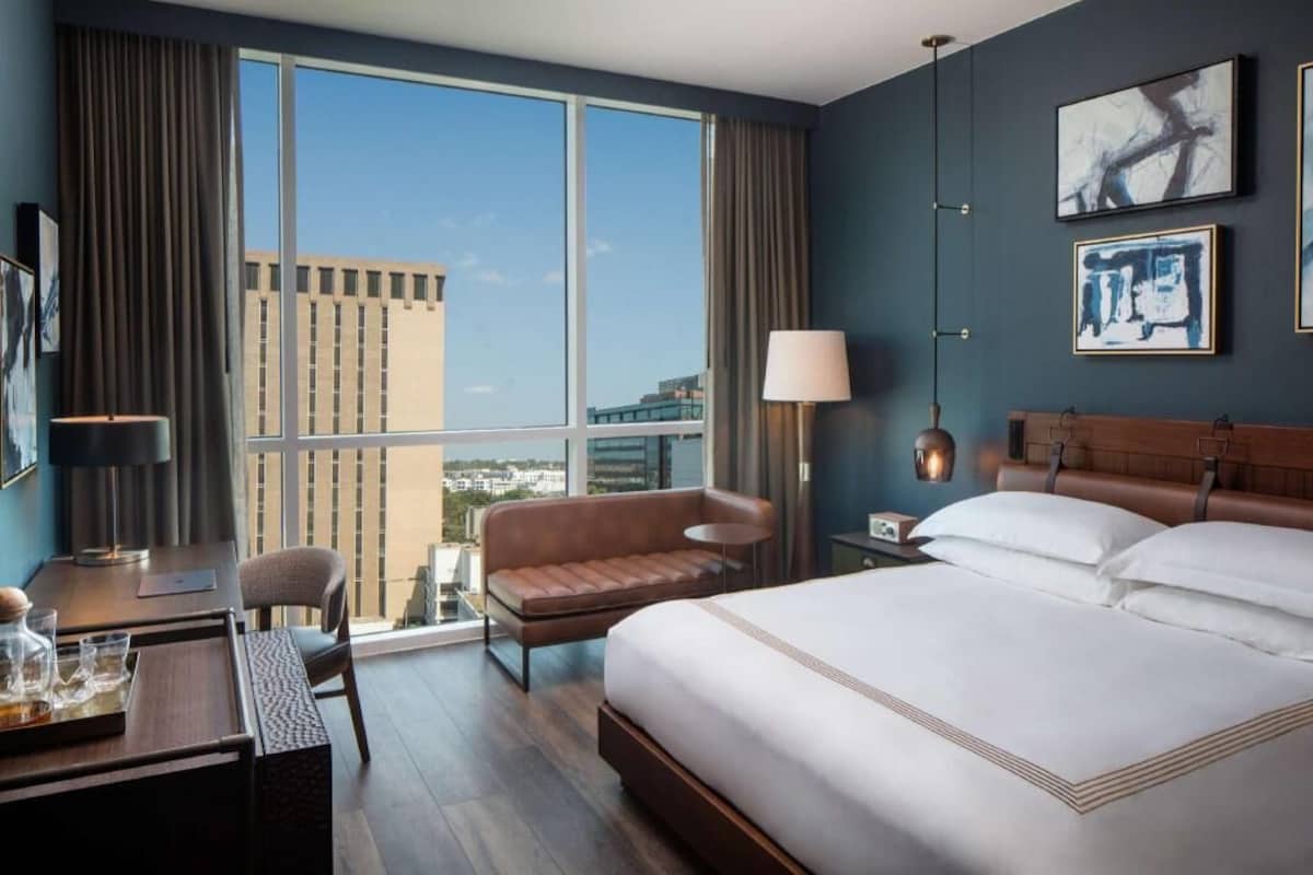 Une chambre d’hôtel avec une grande fenêtre, un lit, un bureau, une chaise et un canapé.