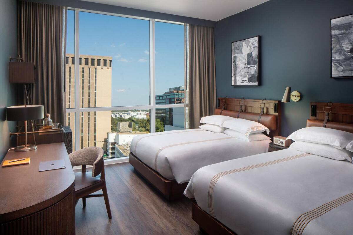 Une chambre d’hôtel avec deux lits, un bureau, une chaise, une lampe et une vue sur la ville.