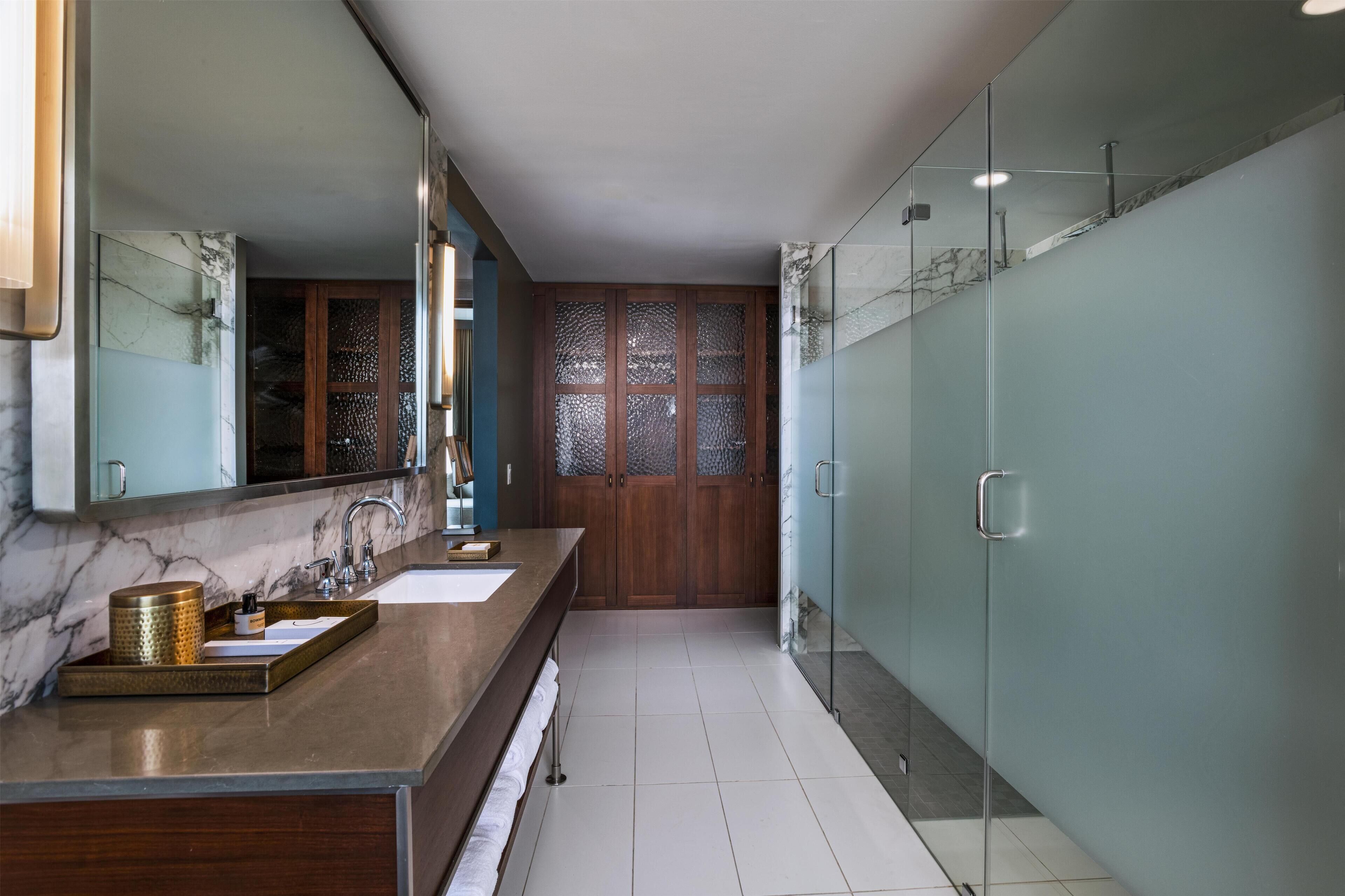 A modern bathroom with a marble countertop, a glass shower enclosure, and a wooden door with frosted glass panels.