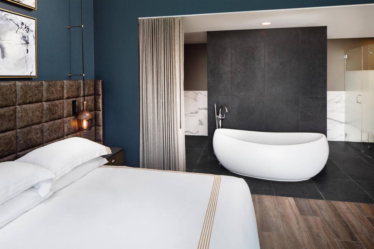 Une chambre d’hôtel moderne avec un grand lit, une baignoire sur pieds et un mur recouvert de carreaux de marbre.