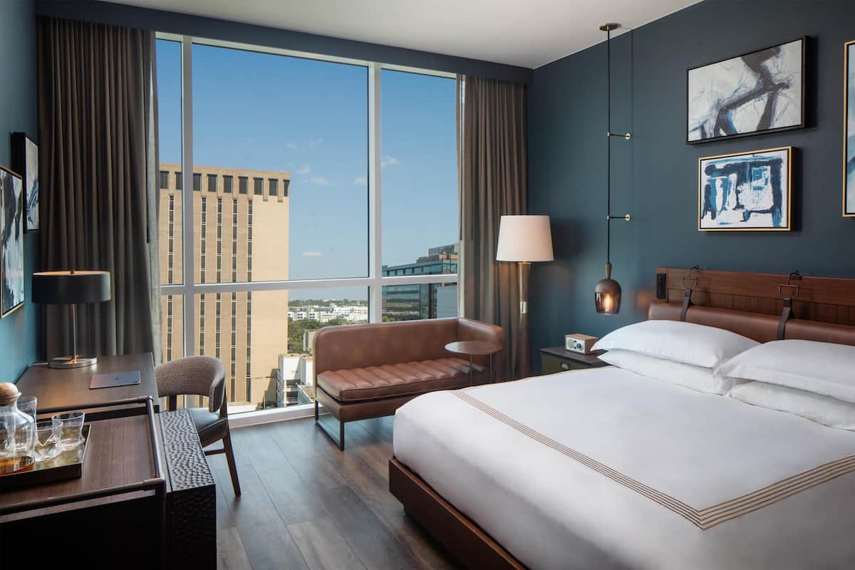 Une chambre d’hôtel avec une grande fenêtre, un lit, un bureau, une chaise et un canapé.