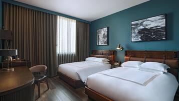A hotel room with two beds, a desk, a chair, and artwork on the walls.