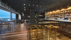 Un bar moderno con una barra larga, varios taburetes y vistas a la ciudad.
