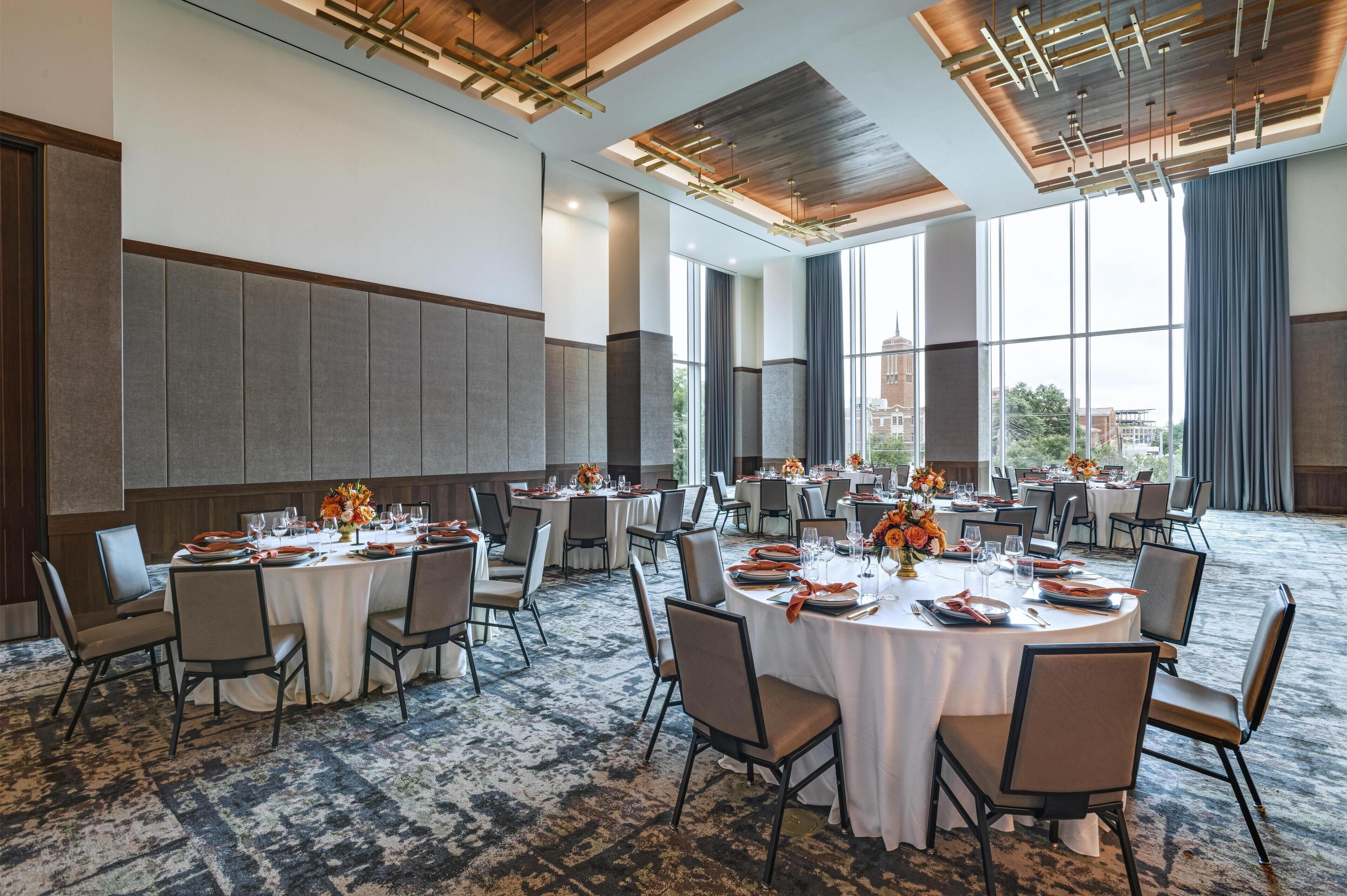 A spacious conference room with round tables, chairs, and a large window offering a view of the cityscape.