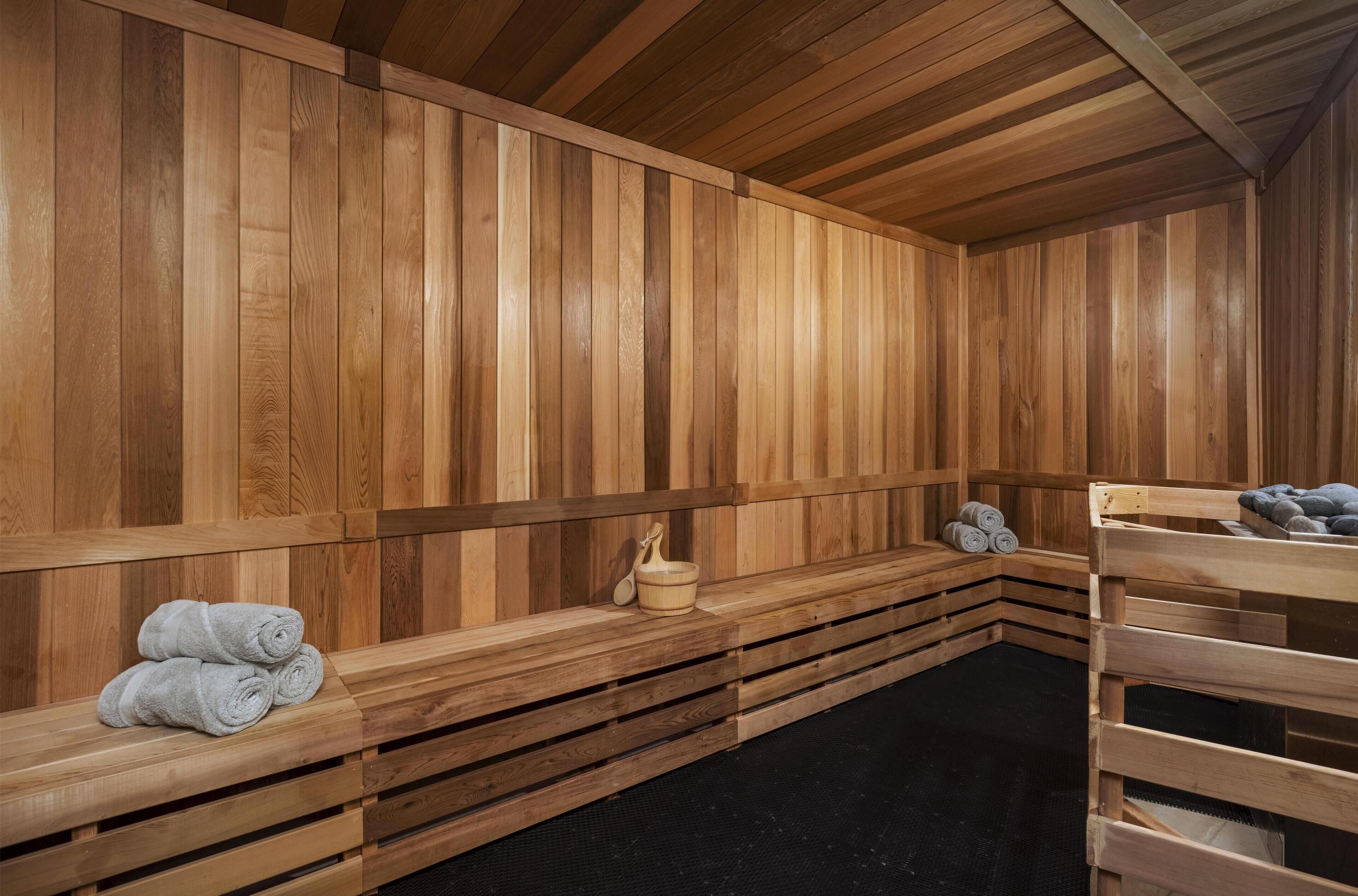 A sauna with wooden benches, a wooden bench with towels, and a wooden bench with a bucket.