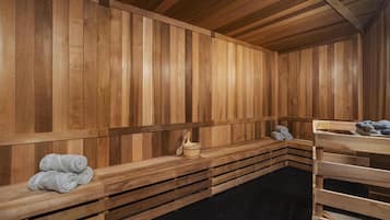 A sauna with wooden benches, a wooden bench with towels, and a wooden bench with a bucket.