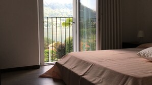 A bedroom with a bed, a nightstand, and a view of a mountain and lake through a sliding glass door.